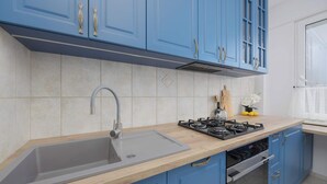 Eine Küche mit blauen Schränken, einem grauen Spülbecken, einer Holzausziehtafel und einem Gasherd.
