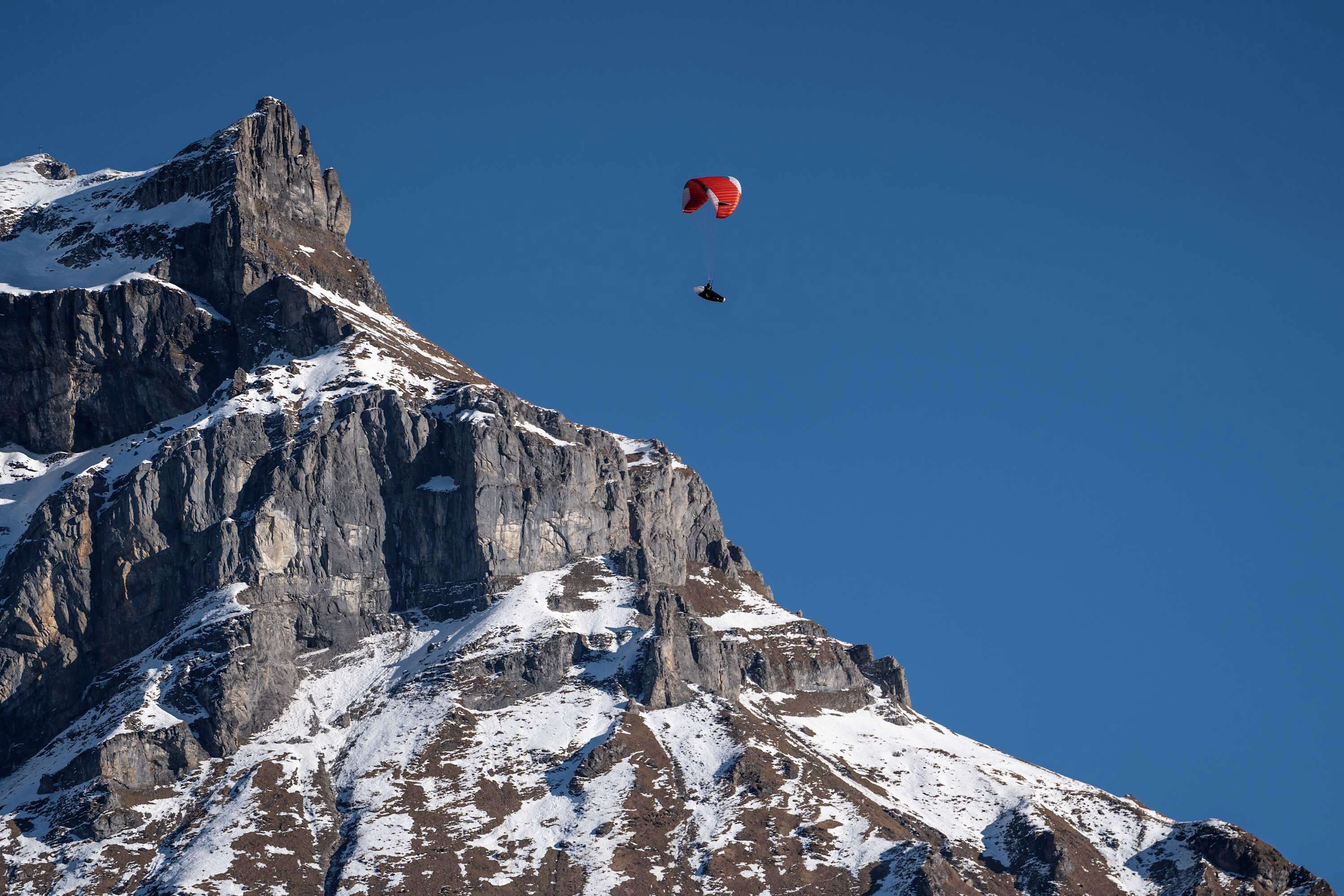 A mountain with a snow-covered peak and a person paragliding in the sky.