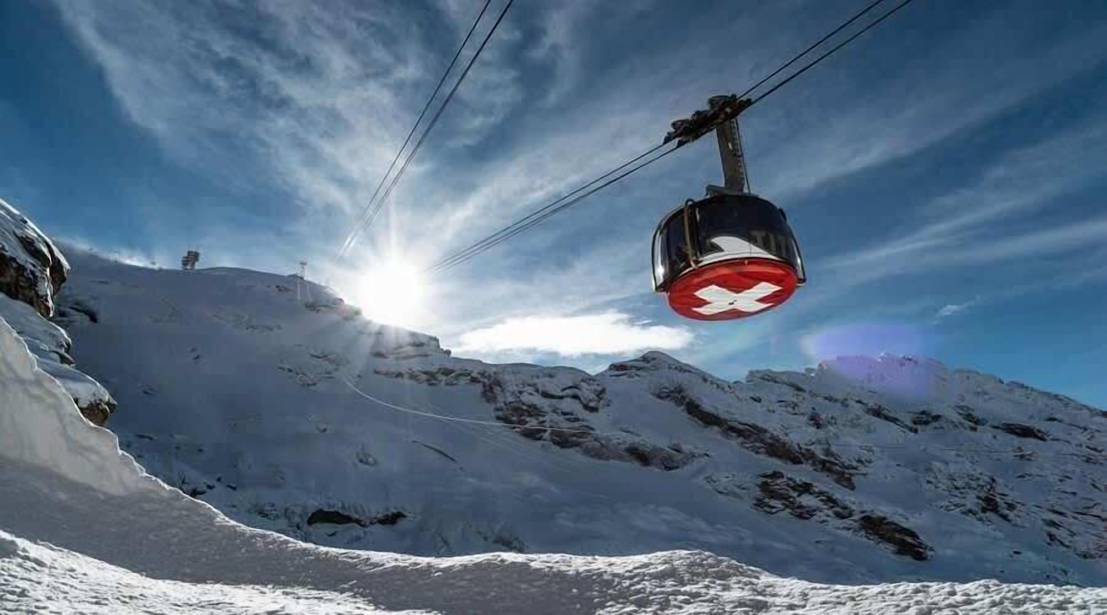 A cable car moving over a snowy mountain with a clear sky.