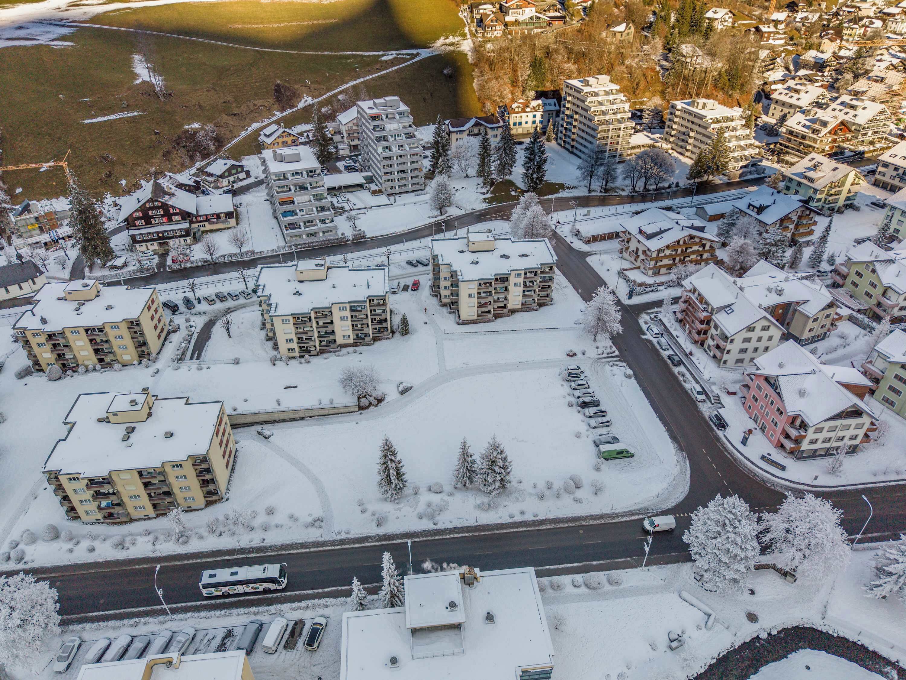 Eine Vogelperspektive auf ein Wohngebiet mit mehreren Mehrfamilienhäusern, Straßen und einem mit Schnee bedeckten Parkplatz.