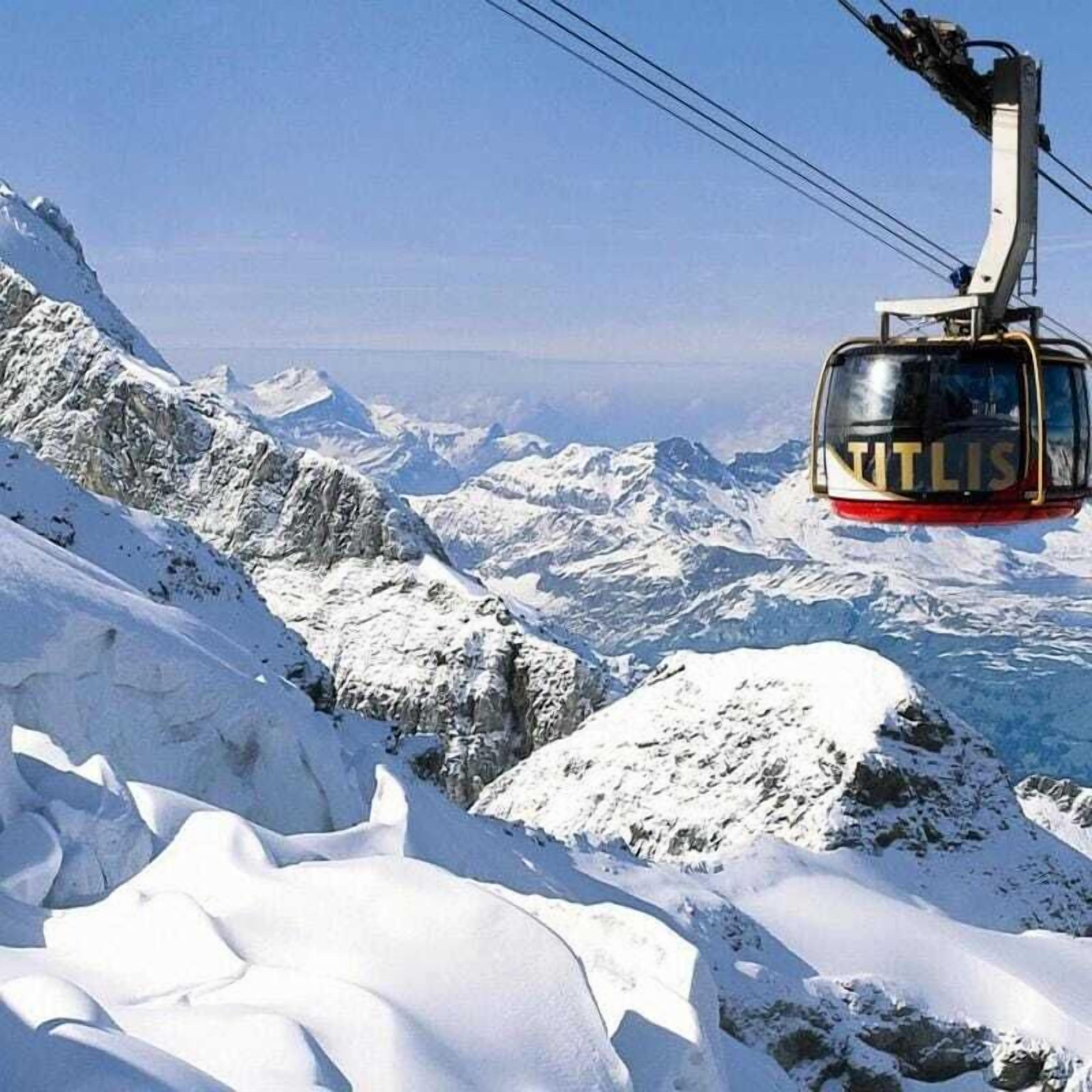 A cable car with "NITLIS" written on it, moving over a snowy mountain landscape.