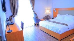 A hotel room with a bed, a desk with a lamp, a chair, and a TV mounted on the wall. - Libanos Hotel (Mek'ele)