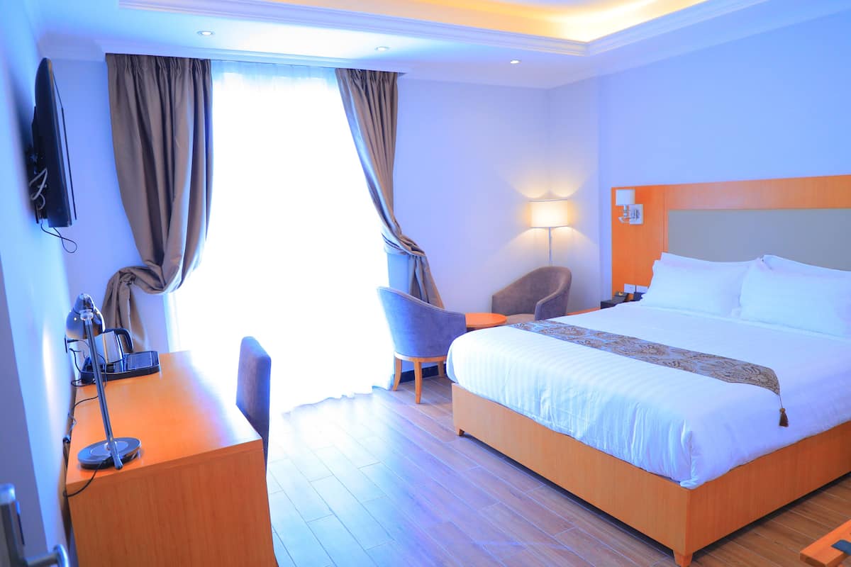 Una habitación de hotel con una cama, un escritorio con lámpara, una silla y un televisor montado en la pared.
