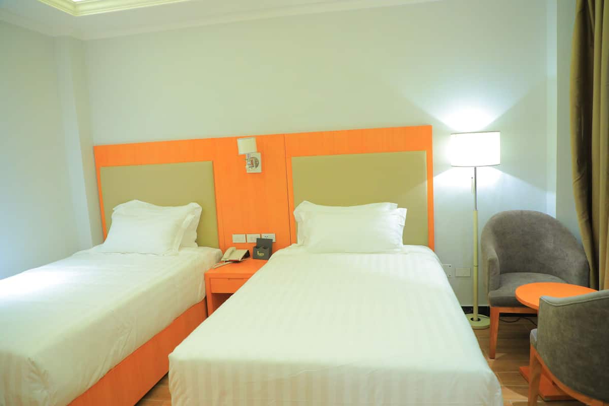 Habitación de hotel con dos camas individuales, una mesita de noche con teléfono y lámpara, y una pequeña mesa con una silla.