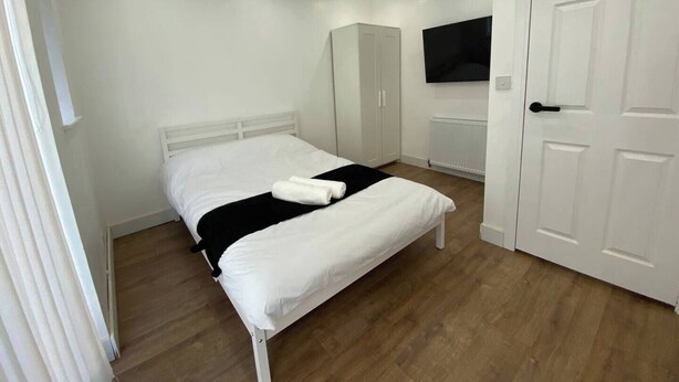 A bedroom with a bed, a wardrobe, a television, and a door. - Luton City Retreat - Spacious 3 Bedroom Apartment (Luton)