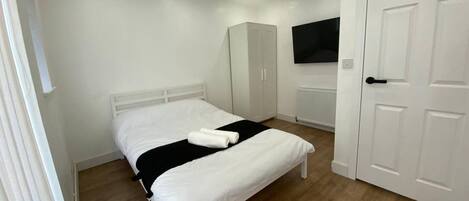 A bedroom with a bed, a wardrobe, a television, and a door.