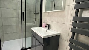 A modern bathroom with a glass shower enclosure, a vanity with a sink, and a towel rack. - Luton City Retreat - Spacious 3 Bedroom Apartment (Luton)