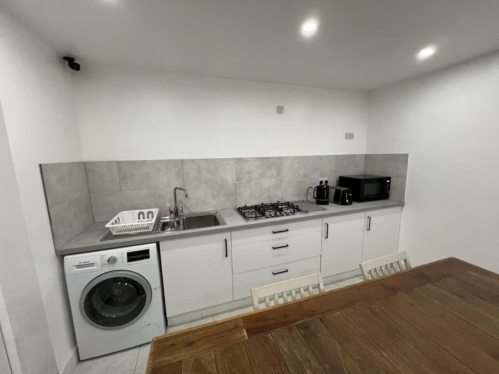 A compact kitchen with a washing machine, sink, stove, and microwave.