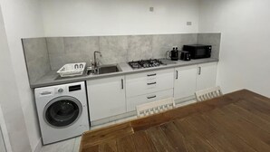 A compact kitchen with a washing machine, sink, stove, and microwave. - Luton City Retreat - Spacious 3 Bedroom Apartment (Luton)