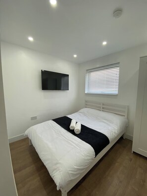 Un dormitorio moderno con cama, televisor de pantalla plana en la pared y ventana con persianas.