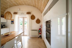 Eine Küche mit einem Holztisch, weißen Stühlen, einem weißen Kühlschrank und einer Decke mit freiliegenden Ziegeln.