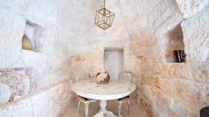 Una habitación de paredes de piedra con una mesa redonda, dos sillas, una lámpara colgante y un estante con libros.