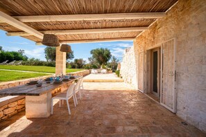 Eine Terrassenausstattung im Freien mit einem Steintisch, Stühlen und einem Reetdach.
