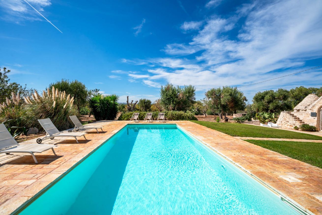 Una piscina rectangular amb aigua clara i blava, envoltada per una terrassa amb rajoles i gandules.