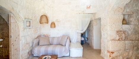 A rustic room with a stone wall, a striped sofa, a wooden coffee table, and a white bench.