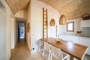 Eine Küche mit Holztisch, weißen Stühlen, einer Leiter und hängenden Lampen aus Weidengeflecht.