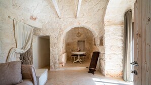 Una habitación rústica con paredes de piedra, una puerta de madera, una mesa blanca con sillas y un sofá.