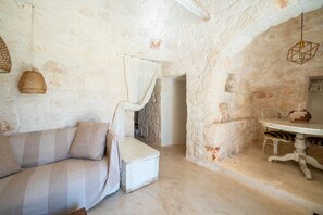 A rustic stone-walled room with a white cushioned sofa, a small table with a woven basket, and hanging light fixtures. - Trullo GiaMar · Private pool in olive grove, 3 bedrooms, dogs welcome · Ostuni (Ostuni)