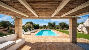 Una piscina exterior techada con suelo de piedra, sillas de descanso y vistas del paisaje circundante.