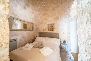 Ein Schlafzimmer mit Steinwänden, einem Bett, Kissen, einem Nachttisch mit Lampe und einem Spiegel.