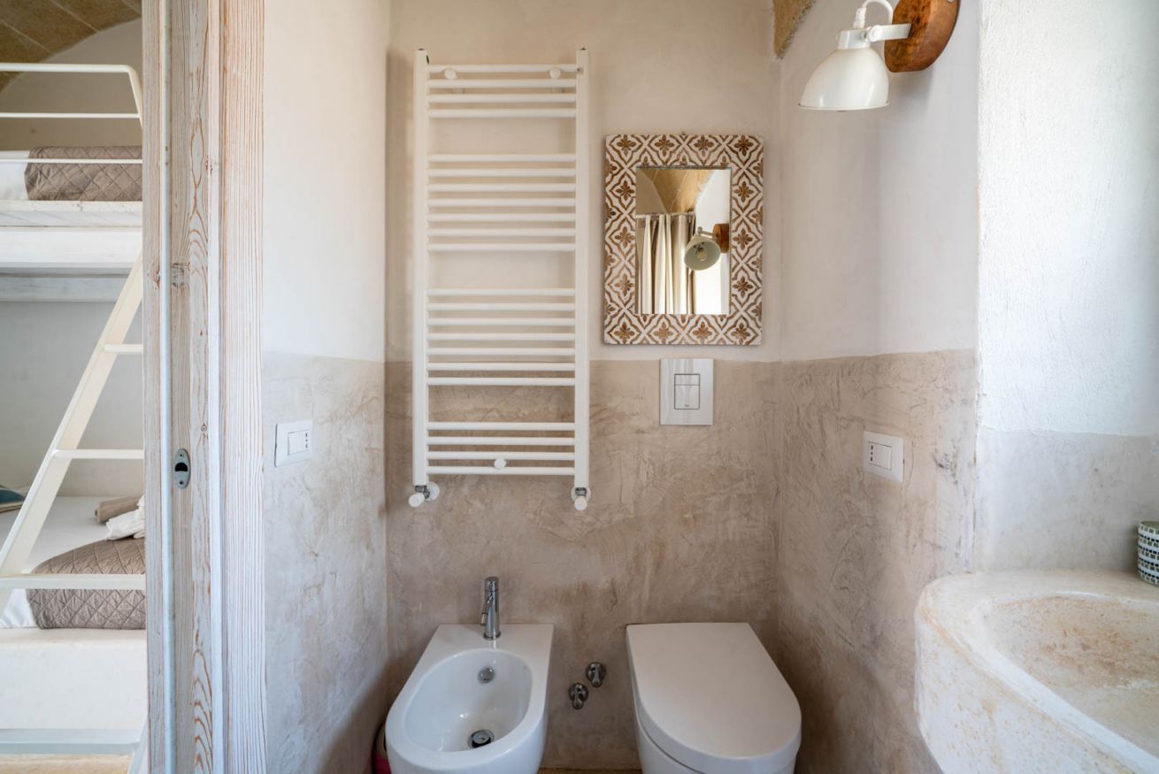 A compact bathroom with a bidet, toilet, towel rack, and a mirror with a decorative frame.