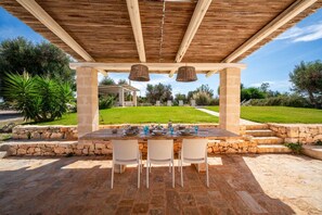 An outdoor dining area with a stone table and chairs, a pergola overhead, and a view of a well-maintained lawn and trees. - Trullo GiaMar · Private pool in olive grove, 3 bedrooms, dogs welcome · Ostuni (Ostuni)