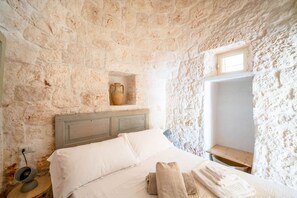 A stone-walled bedroom with a bed, a nightstand, a small table, and a window. - Trullo GiaMar · Private pool in olive grove, 3 bedrooms, dogs welcome · Ostuni (Ostuni)