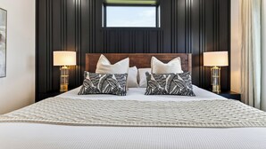 A bedroom with a large bed, two bedside lamps, a window, and a wooden ceiling.