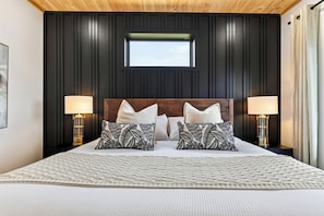 A bedroom with a large bed, two bedside lamps, a window, and a wooden ceiling.
