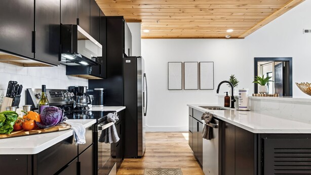 A modern kitchen with dark cabinetry, stainless steel appliances, and a wooden ceiling.
