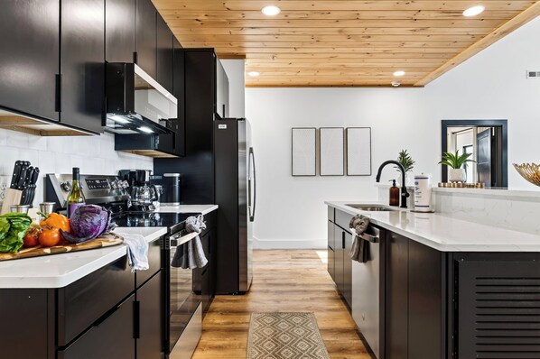 A modern kitchen with dark cabinetry, stainless steel appliances, and a wooden ceiling.