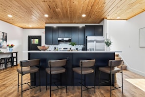 Une cuisine moderne avec des meubles de couleur sombre, un îlot central doté de tabourets de bar et un plafond en bois.