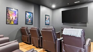 A home theater room with reclining chairs, a large flat-screen TV, and movie posters on the wall.