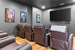 A home theater room with reclining chairs, a large flat-screen TV, and movie posters on the wall.