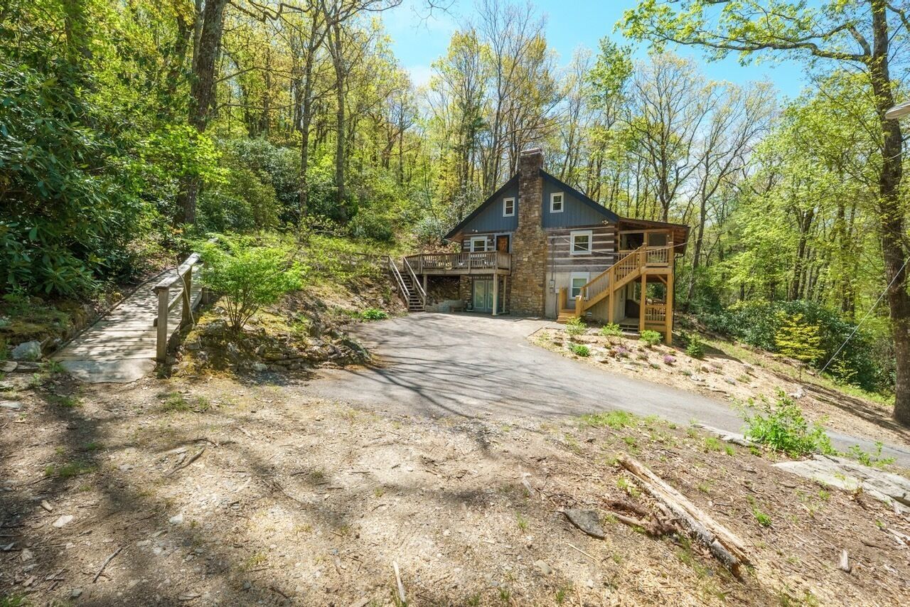 A cabin with a stone exterior, a wooden deck, and a staircase leading to a second level.