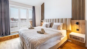 Une chambre moderne avec un grand lit, une table de chevet, un mur revêtu de panneaux en bois et une vue sur le balcon.