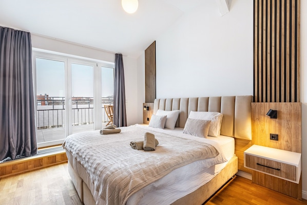 Une chambre moderne avec un grand lit, une table de chevet, un mur revêtu de panneaux en bois et une vue sur le balcon.