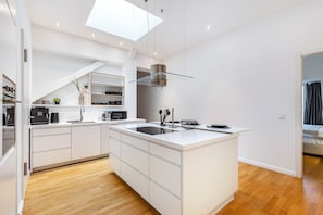 Une cuisine moderne avec des meubles blancs, un îlot central, une verrière et un four encastré.
