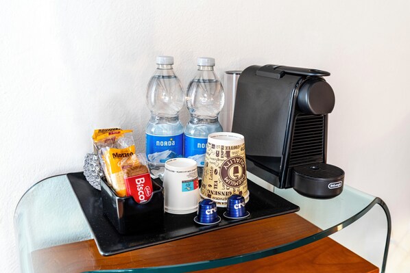 A glass table with a coffee maker, two water bottles, a coffee cup, a biscotti bag, a biscotti box, and two creamer cups. - Locanda Art Deco' (Venice)