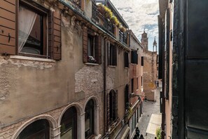 A narrow street with buildings featuring arched windows and balconies with hanging plants. - Locanda Art Deco' (Venice)