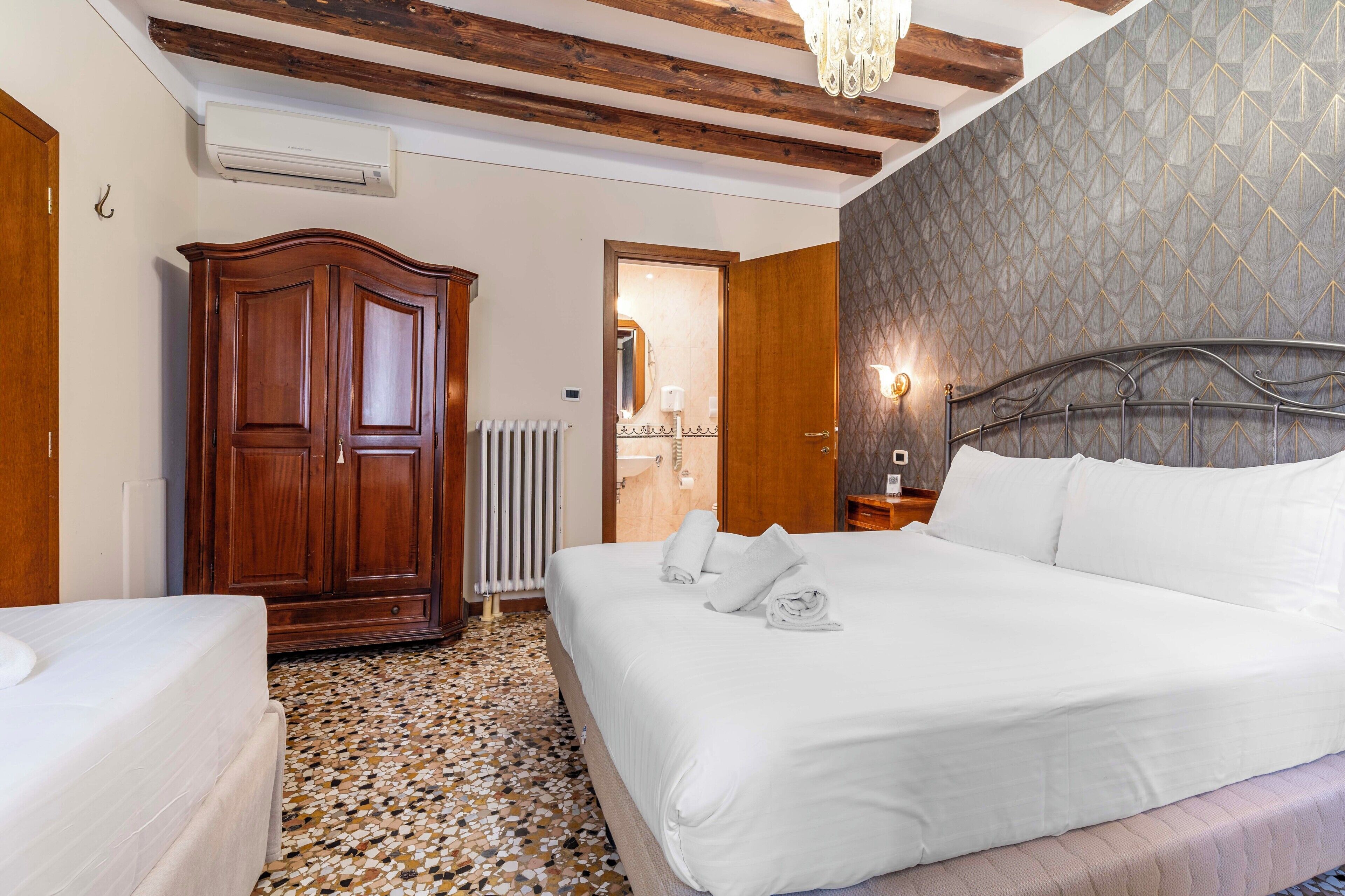A hotel room with a bed, a wardrobe, a radiator, and a chandelier.