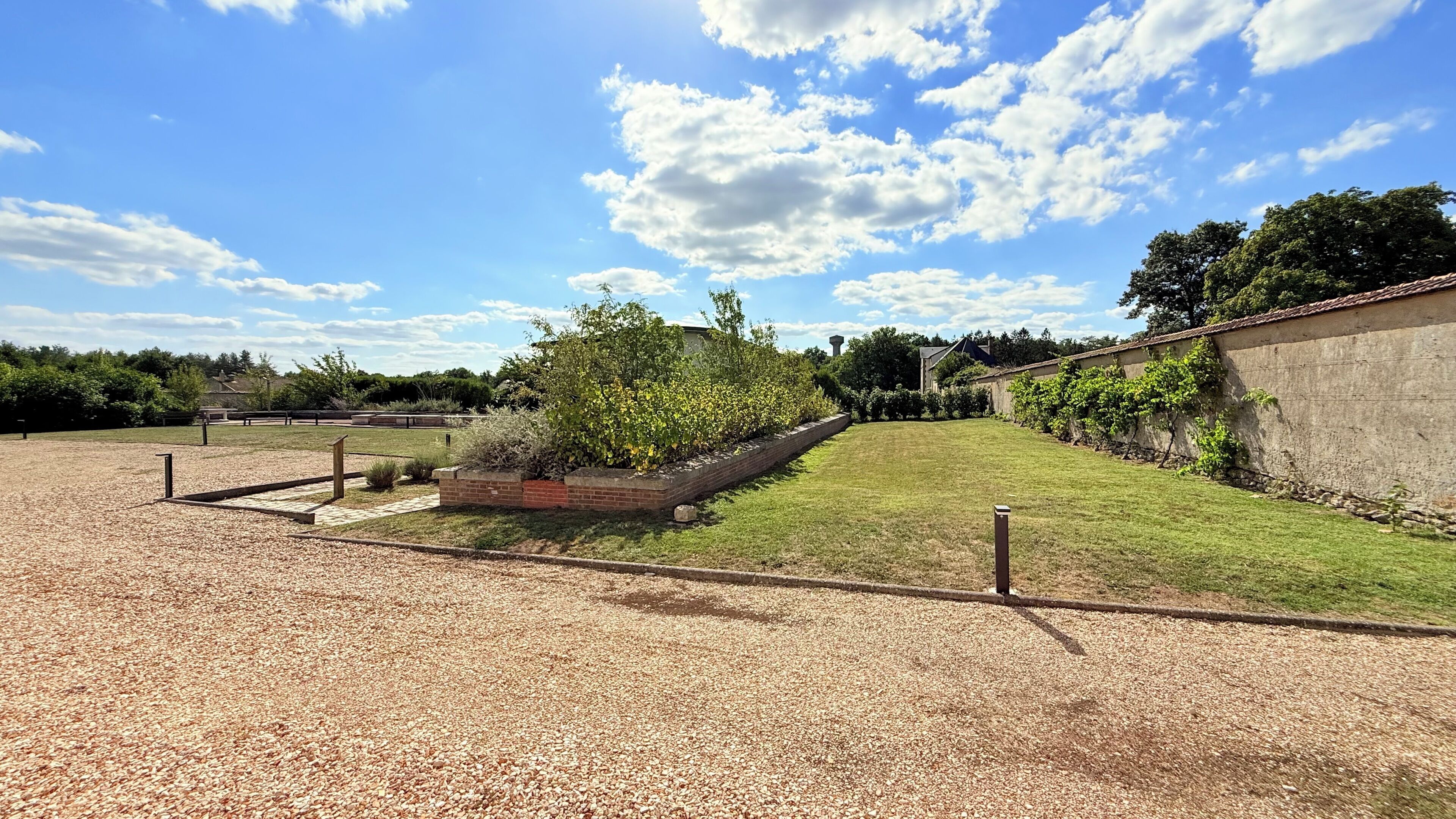 A gravel area with a paved path, a grassy lawn, and a brick planter with plants.
