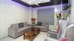 A modern living room with two grey sofas, a wooden coffee table, and a ceiling fan. - The Ashoka Hotel (Bareilly)