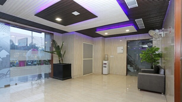 A modern lobby with a glass partition, a reception desk, a staircase, and a seating area. - The Ashoka Hotel (Bareilly)