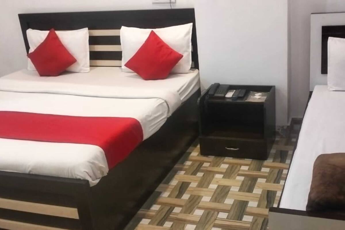 Une chambre d’hôtel avec deux lits, l’un recouvert d’une couvre-lit rouge et blanche, et l’autre d’une couvre-lit blanche. Le sol est en bois et il y a une petite table de chevet avec une lampe et un téléphone.