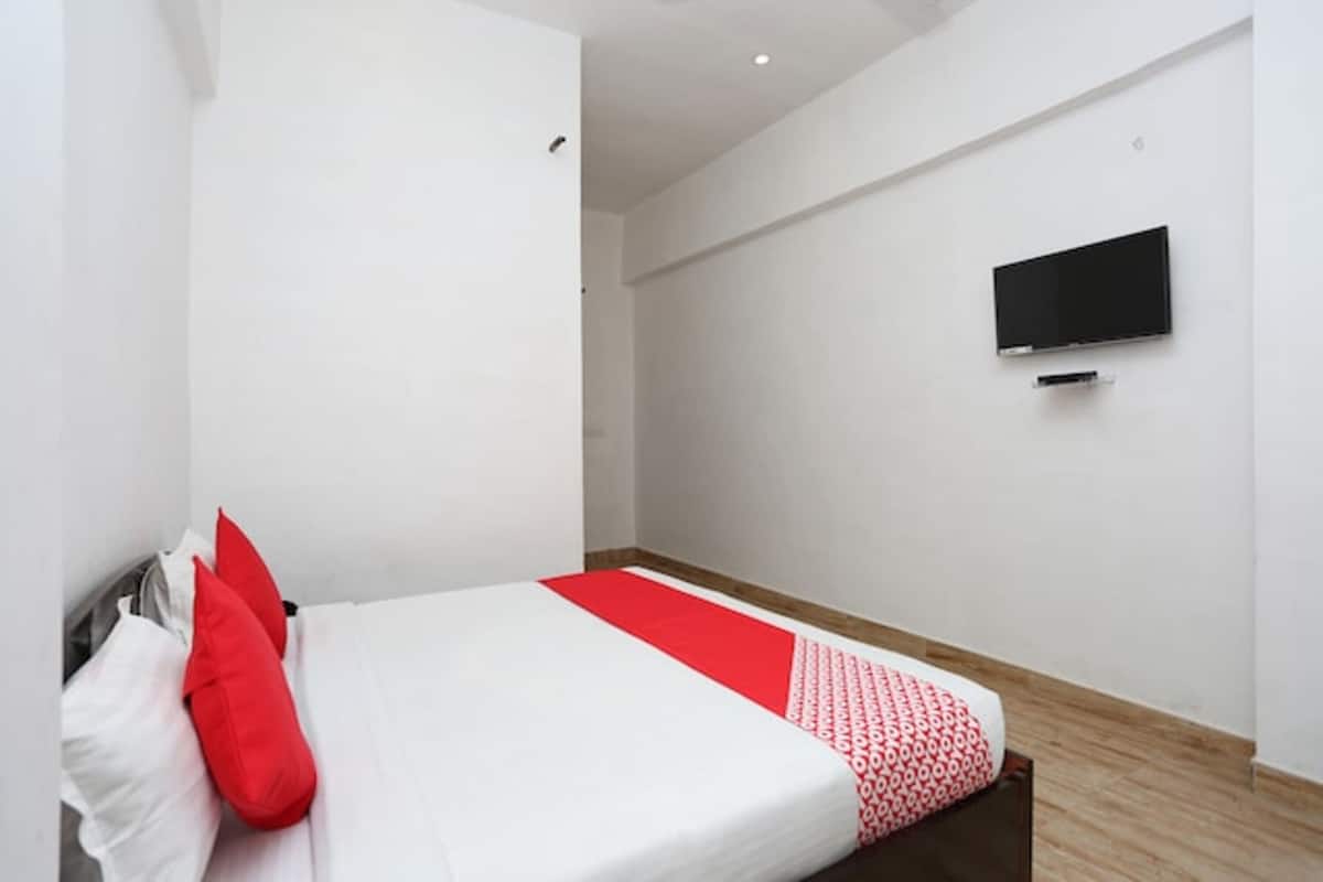 Un lit simple avec une literie rouge et blanche, un téléviseur à écran plat fixé au mur et un plancher en bois.
