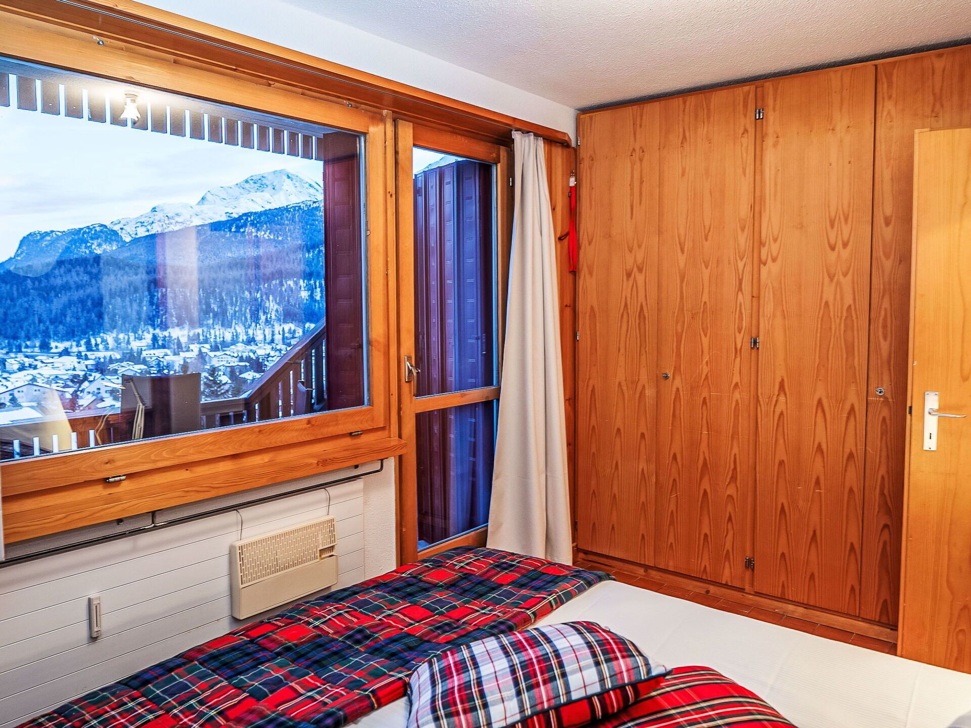 Ein Schlafzimmer mit einem Bett, einem Fenster mit Blick auf einen verschneiten Berg und einem Holzschrank.