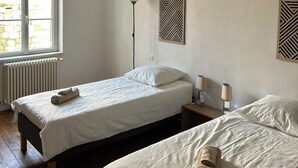 A hotel room with two single beds, a standing lamp, and a radiator.