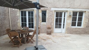 An outdoor patio with a table and chairs, a metal umbrella, and a stone wall.