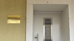 A white door with a handle and a peephole, a small black intercom, and a sign above the door reading "HOSTEL PULSE ul. Powstańców Śląskich 20B, 01-381 Warszawa". - HOSTEL PULSE (Warsaw)